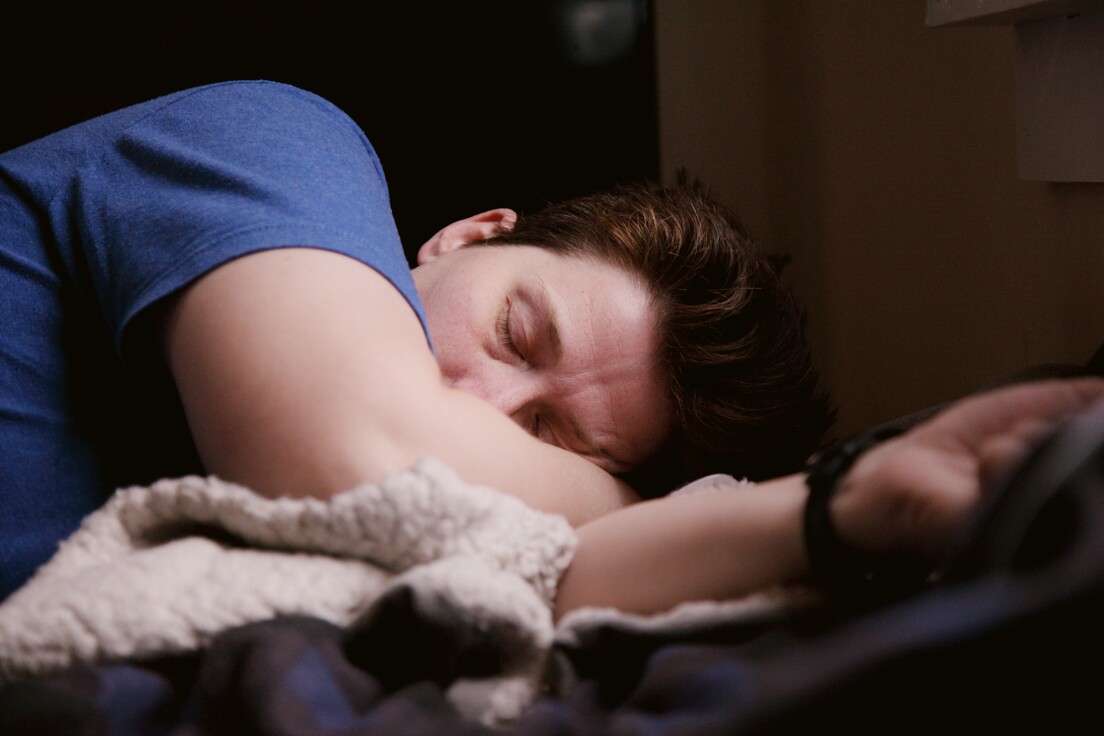 Mann in blauem T-Shirt liegt seitlich im Bett und schläft. 