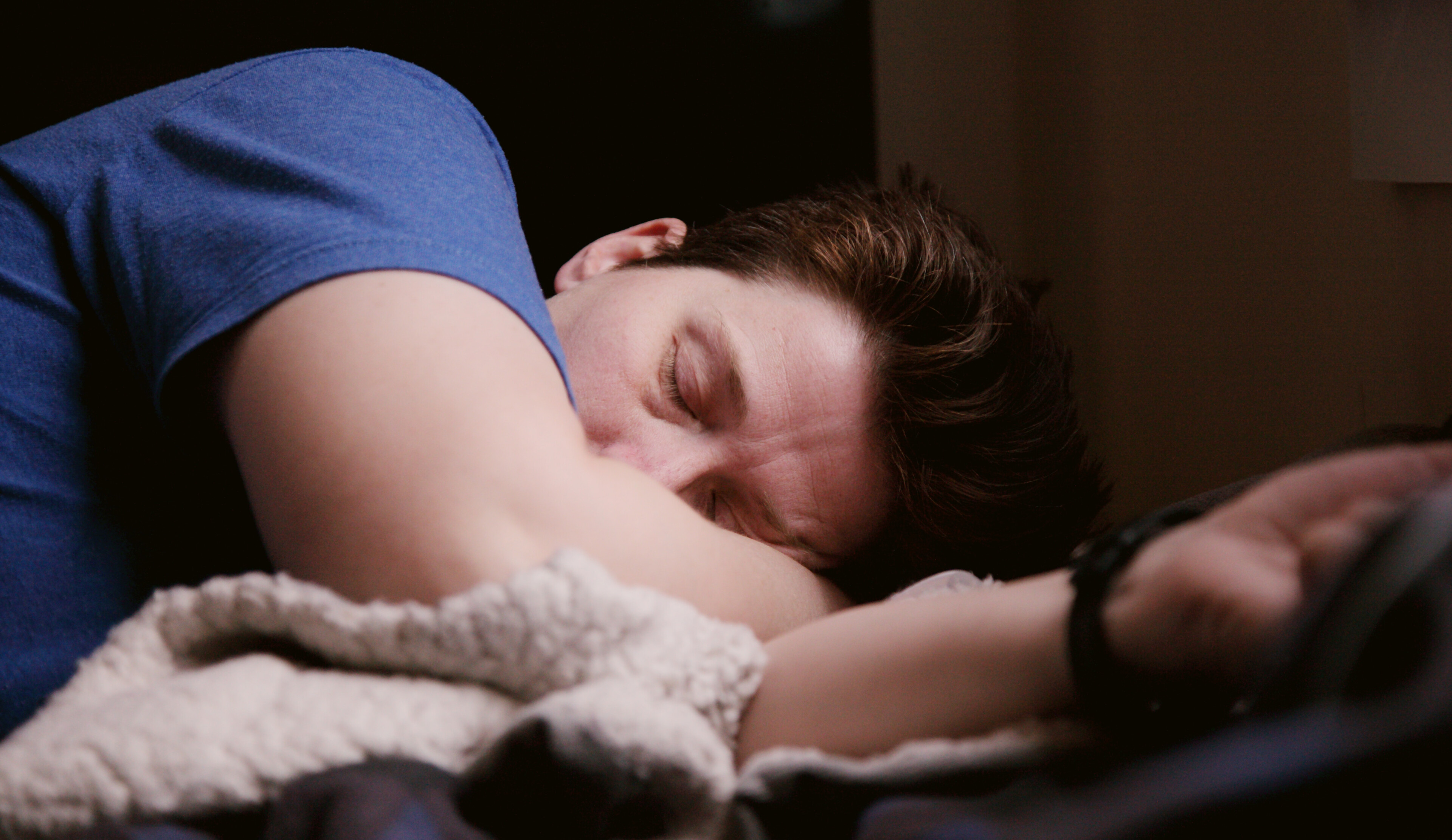 Mann in blauem T-Shirt liegt seitlich im Bett und schläft. 