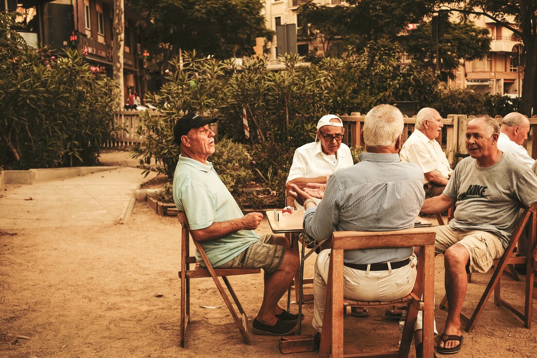 Menschen sitzen bei gutem Wetter draußen am Tisch und unterhalten sich.